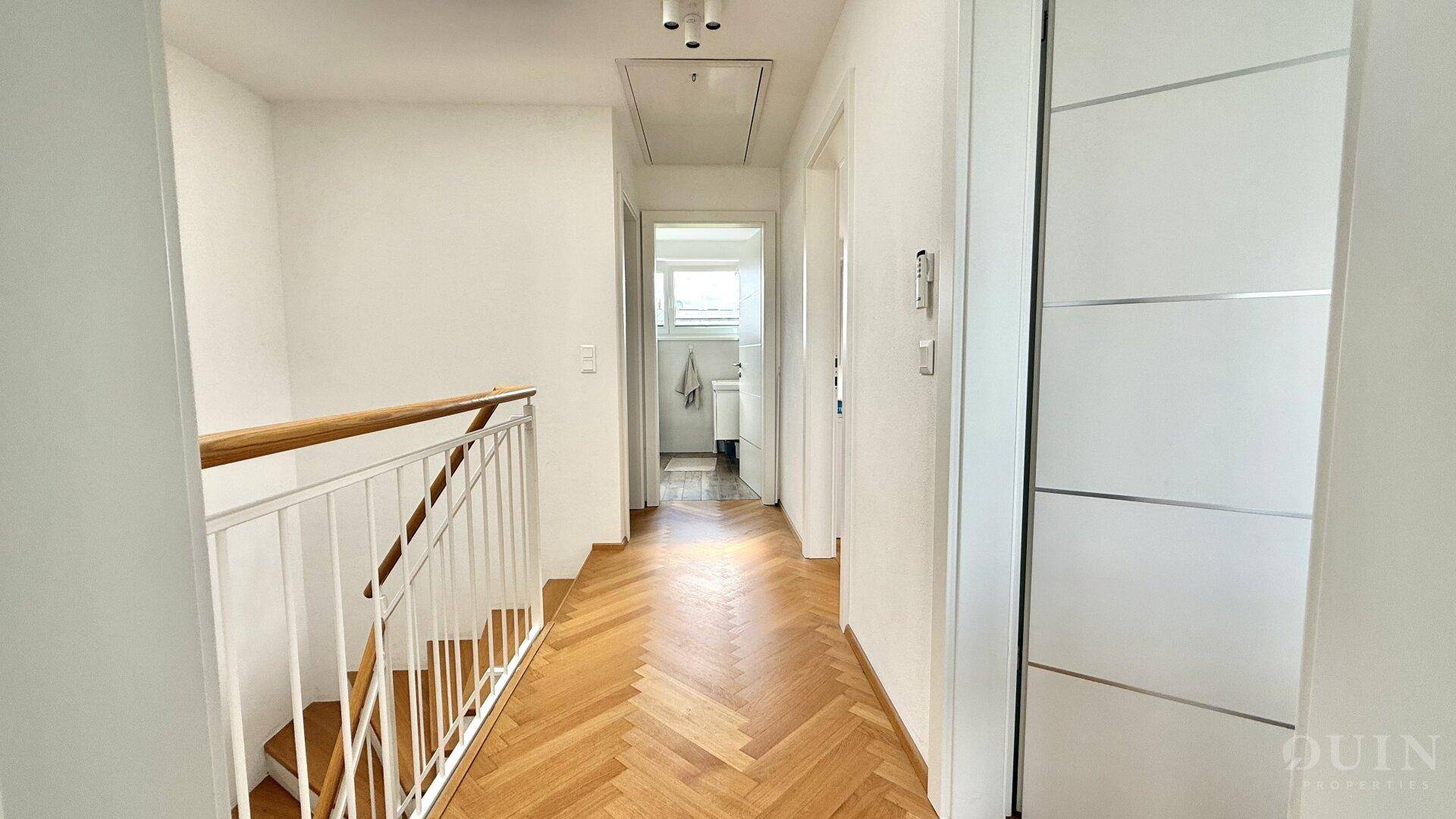 Flur im Obergeschoss mit Parkettboden, Treppengeländer und Zugang zu einem Badezimmer.