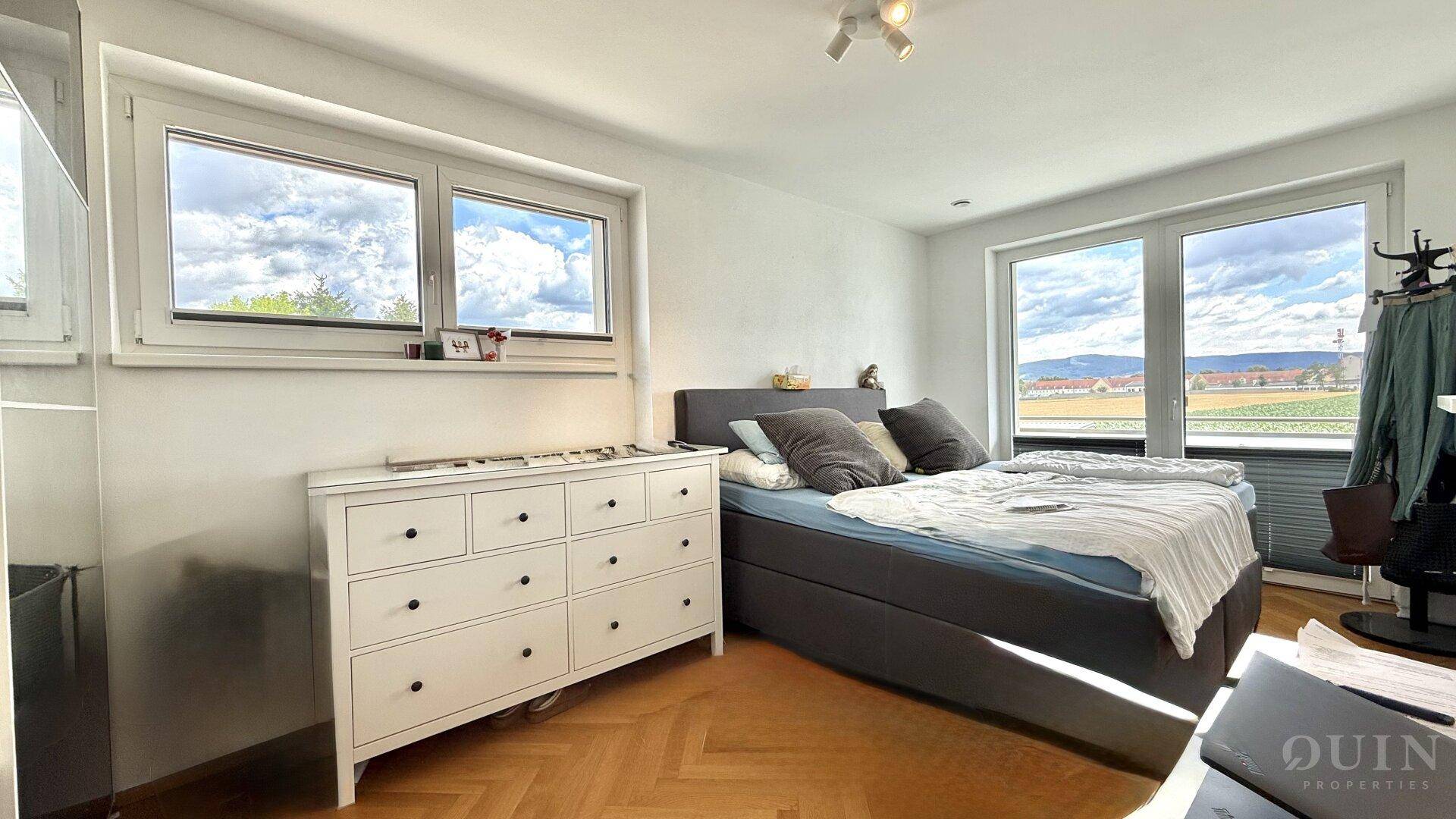 Geräumiges Schlafzimmer mit Bett, Kommode und weitem Blick über die Landschaft.