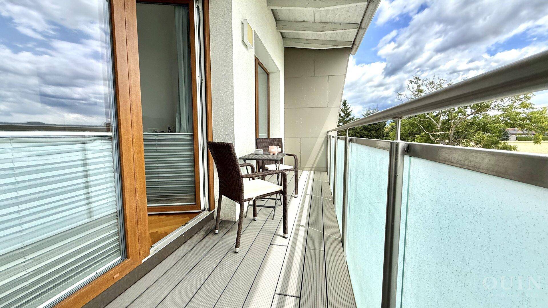 Kleiner Balkon mit Sitzgelegenheiten und Zugang durch eine große Glastür.
