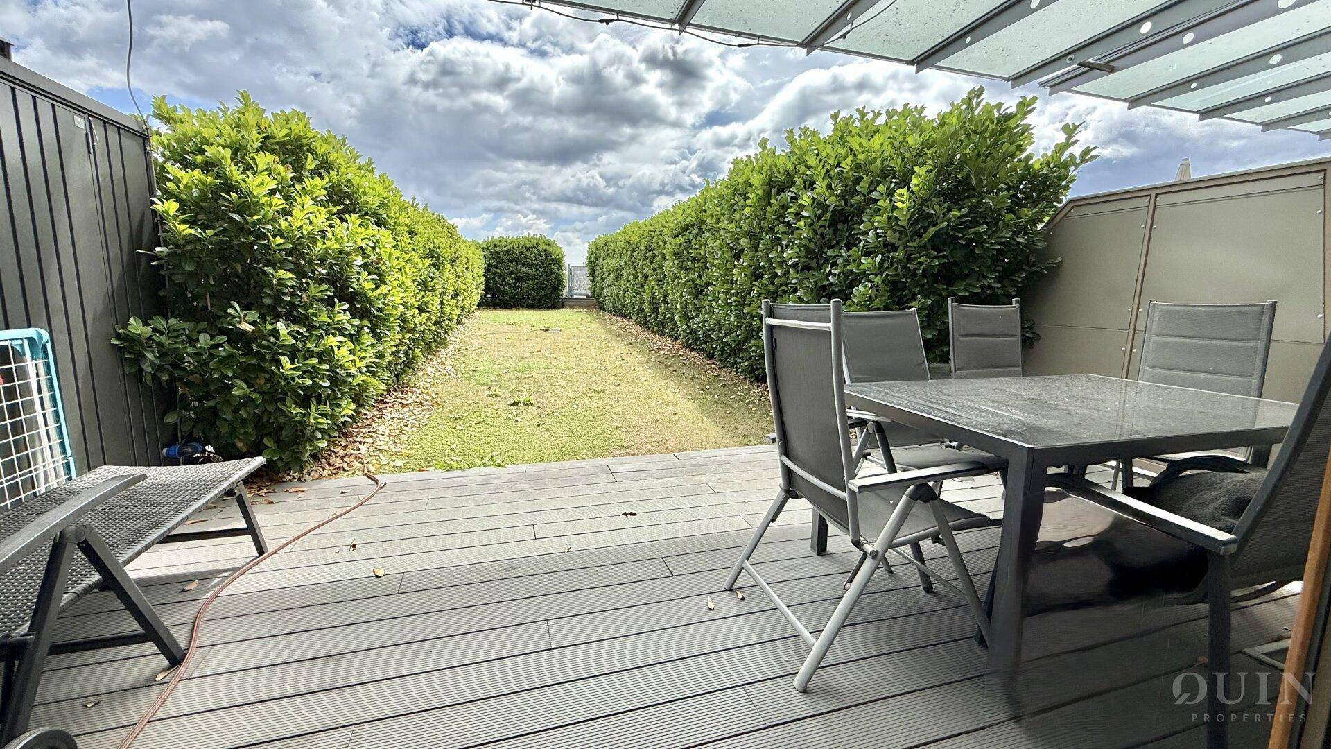 Geräumige Terrasse mit Gartenmöbeln, umgeben von Hecken und Blick auf eine Rasenfläche.