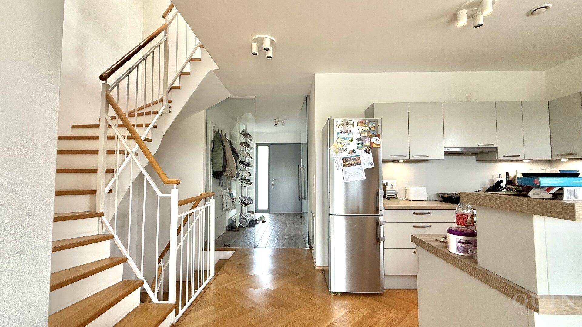 Heller Eingangsbereich mit Treppe, Garderobe und Blick auf die offene Küche.