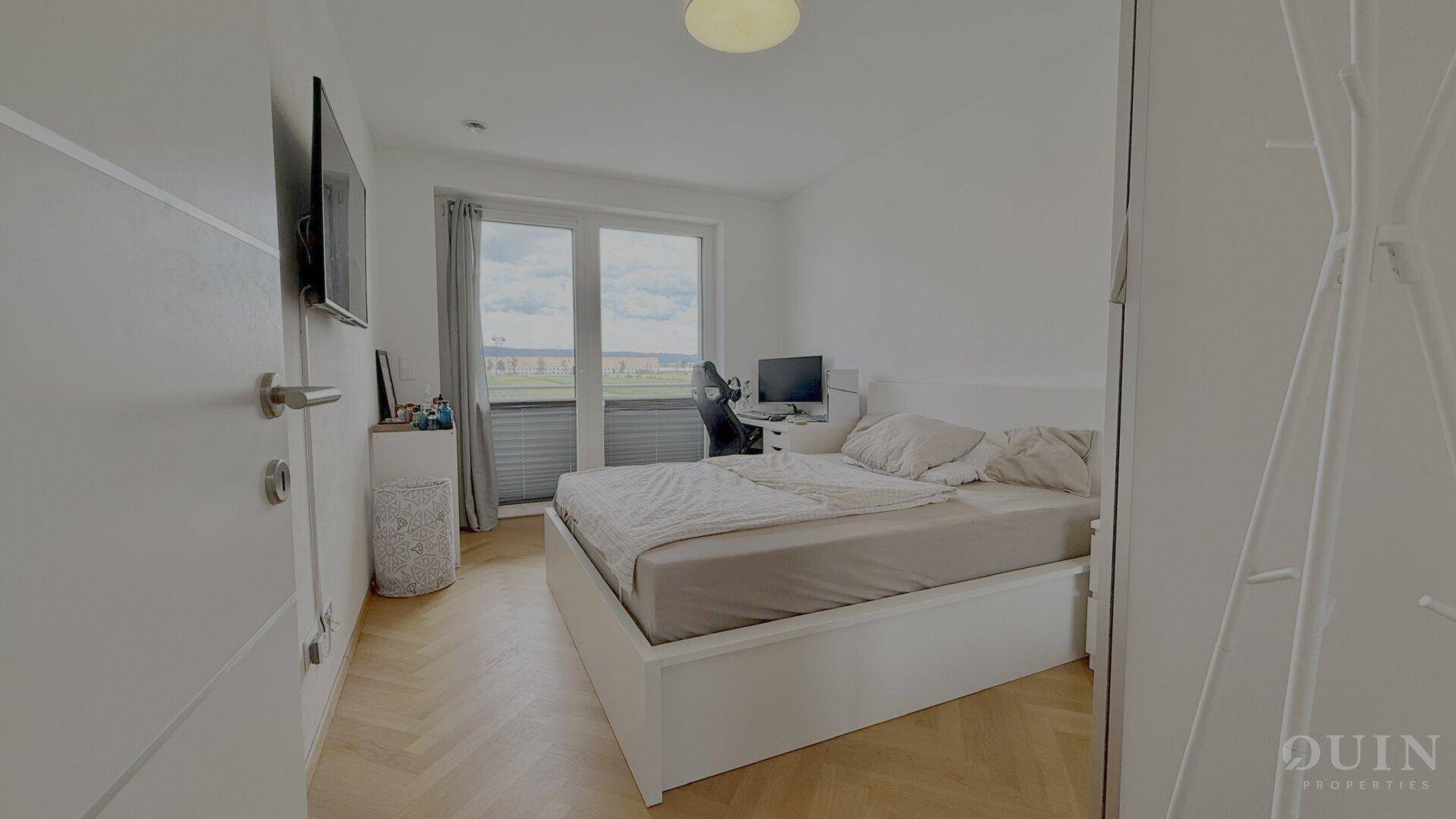 Schlafzimmer mit Bett, Schreibtisch und Zugang zu einem Balkon oder einer Terrasse.