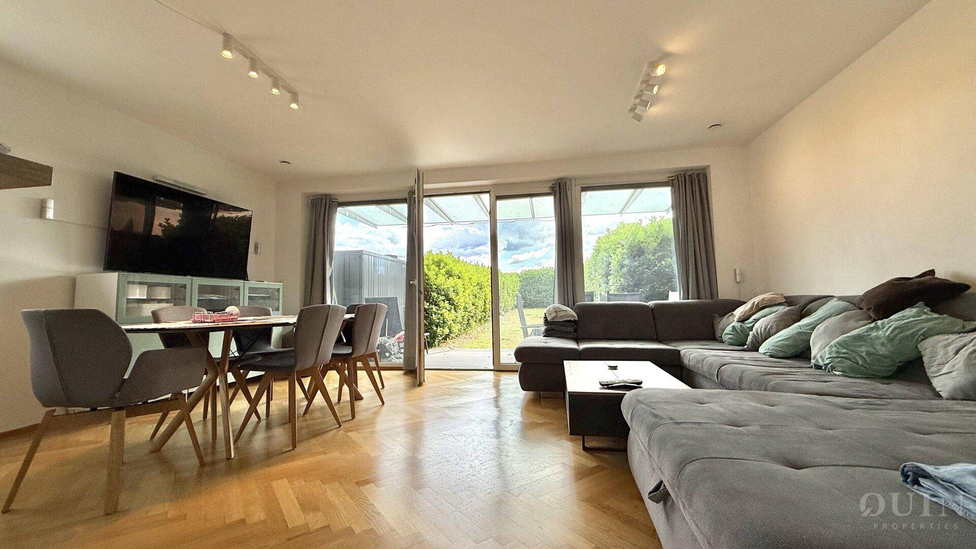 Heller Wohn- und Essbereich mit großem Sofa, Esstisch und Zugang zur Terrasse.