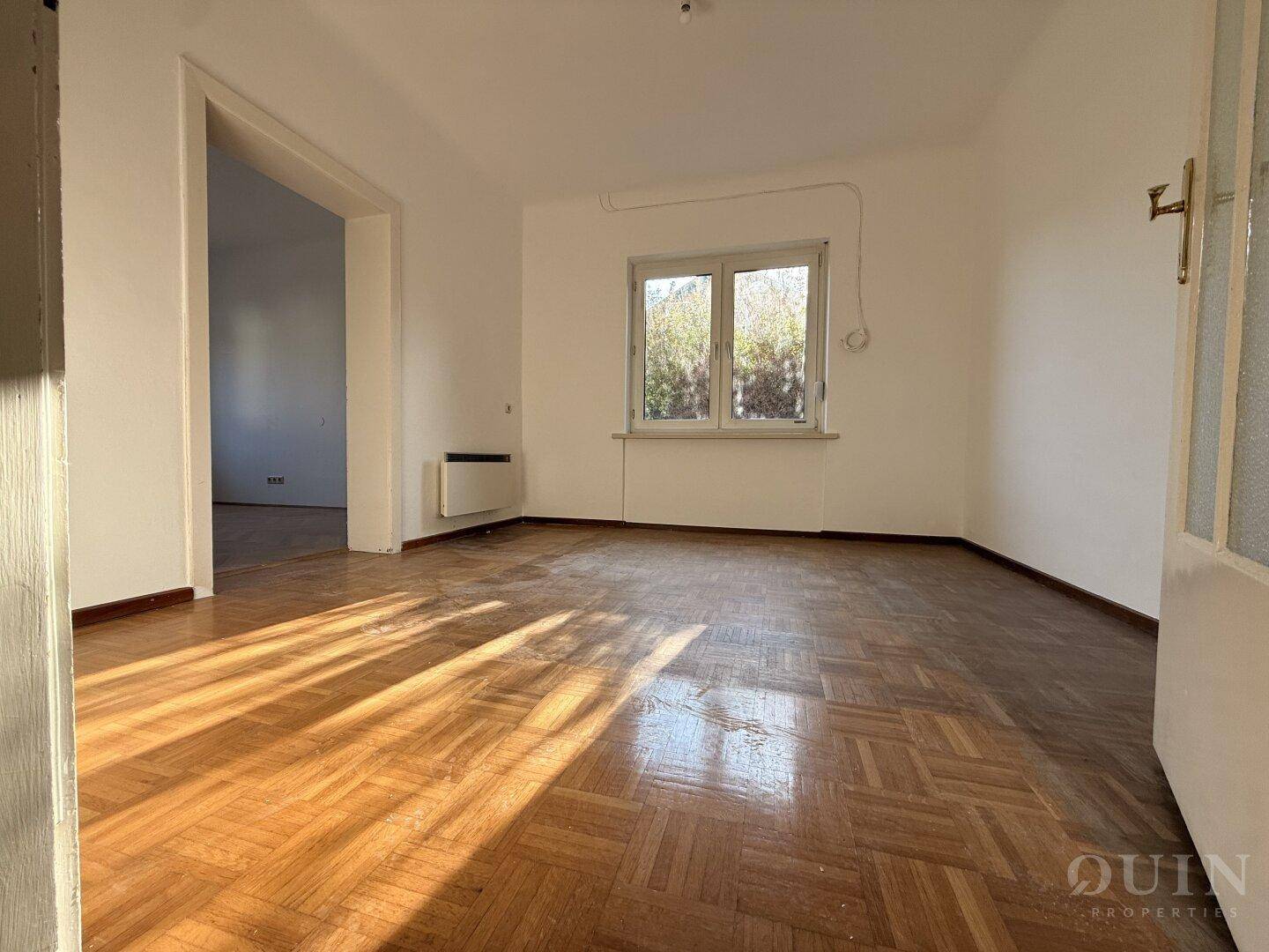 Helles Wohnzimmer mit Fischgrätparkett und Fenster mit Blick ins Grüne.