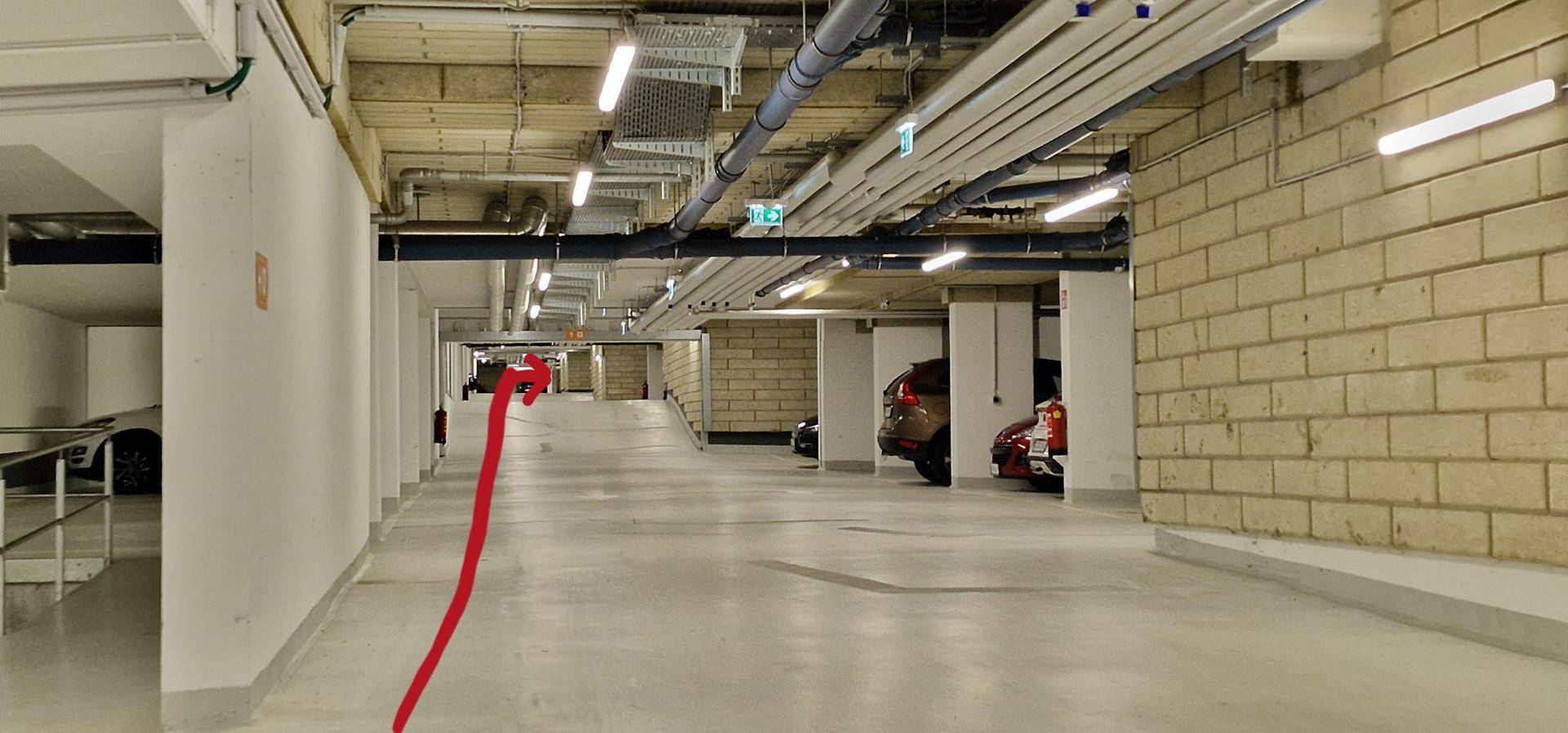 Helle und geräumige Tiefgarage mit mehreren Stellplätzen und sichtbaren Installationen an der Decke.
