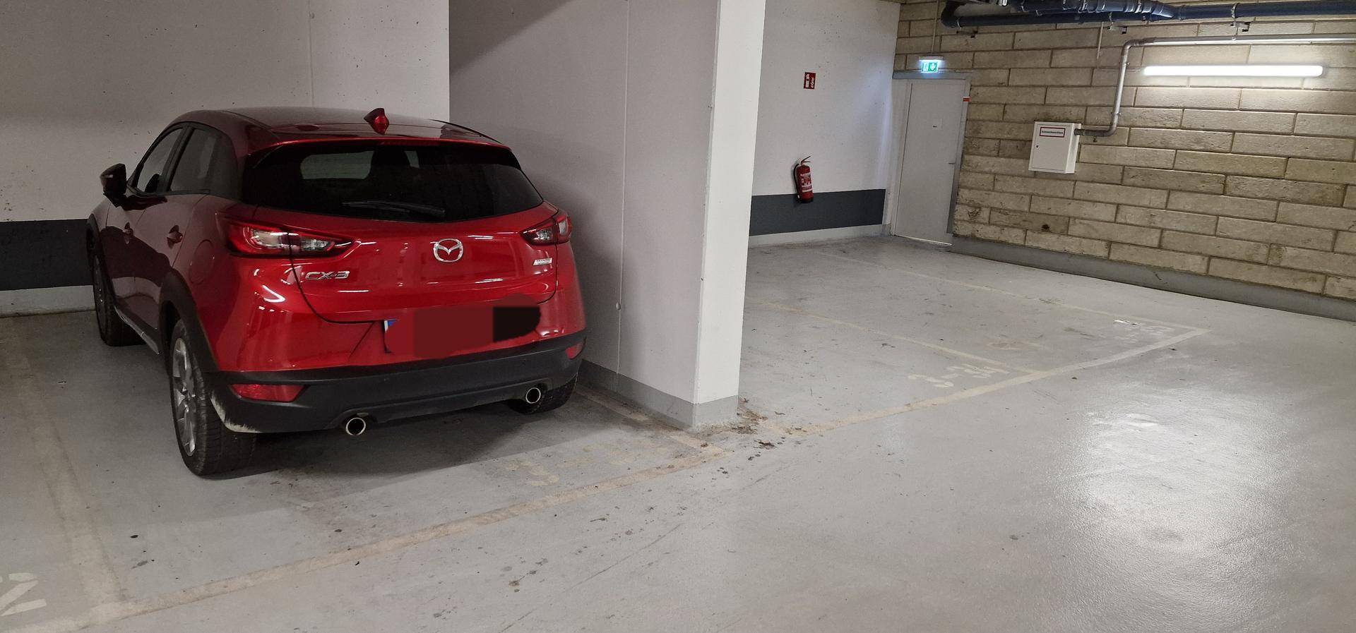 Einzelner Stellplatz in einer sauberen Tiefgarage mit einem roten Fahrzeug.