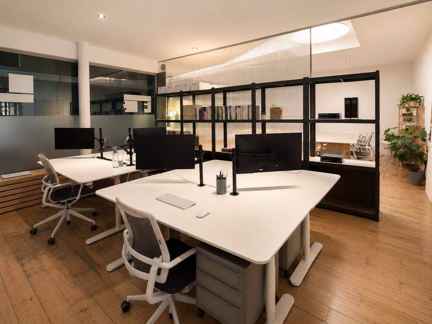 Modernes Büro mit mehreren Arbeitsplätzen, ergonomischen Stühlen und einem Regal als Raumteiler.