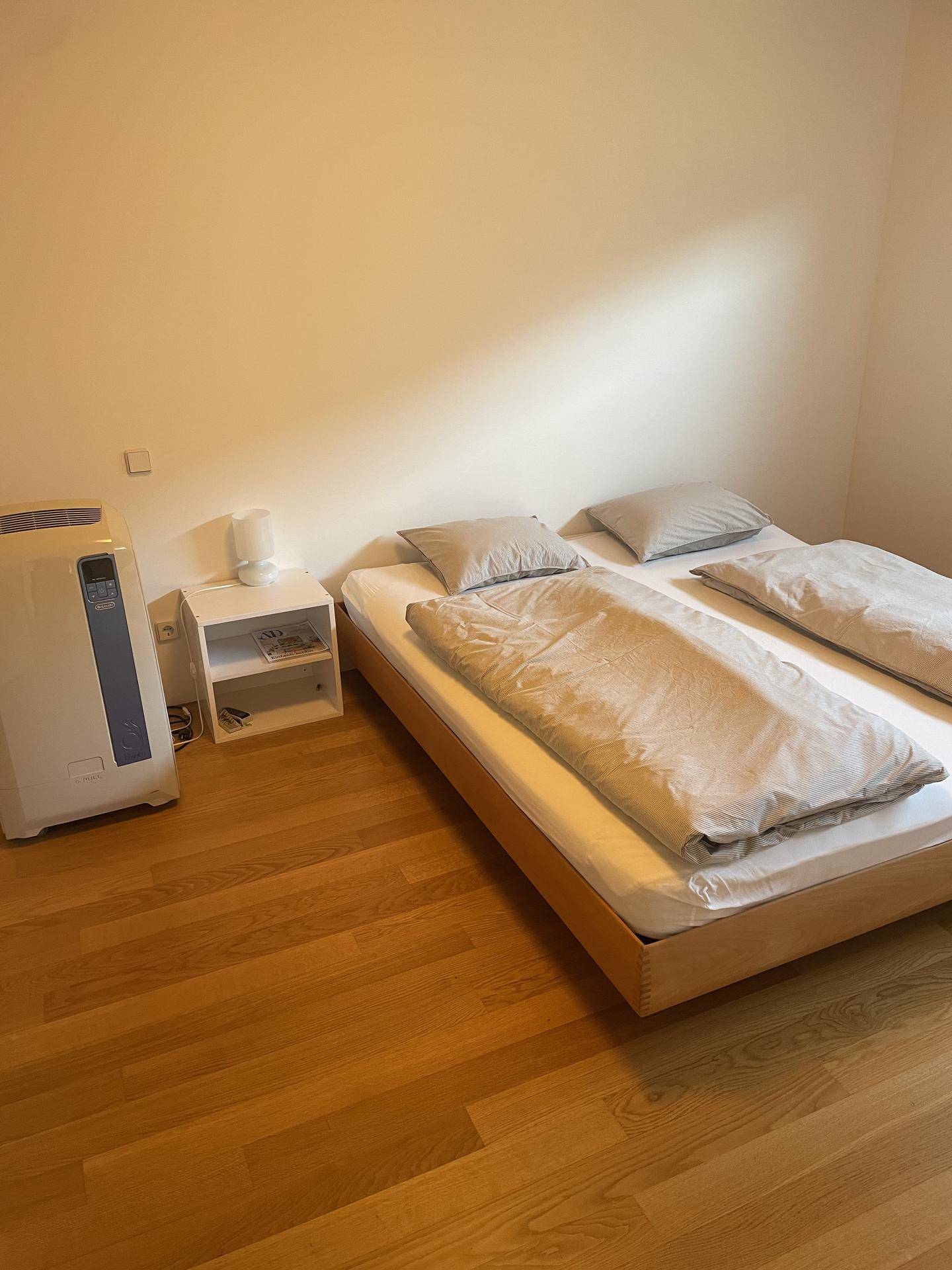 Schlafzimmer mit Holzbett, Nachttisch und einem Luftreiniger, gut beleuchtet.