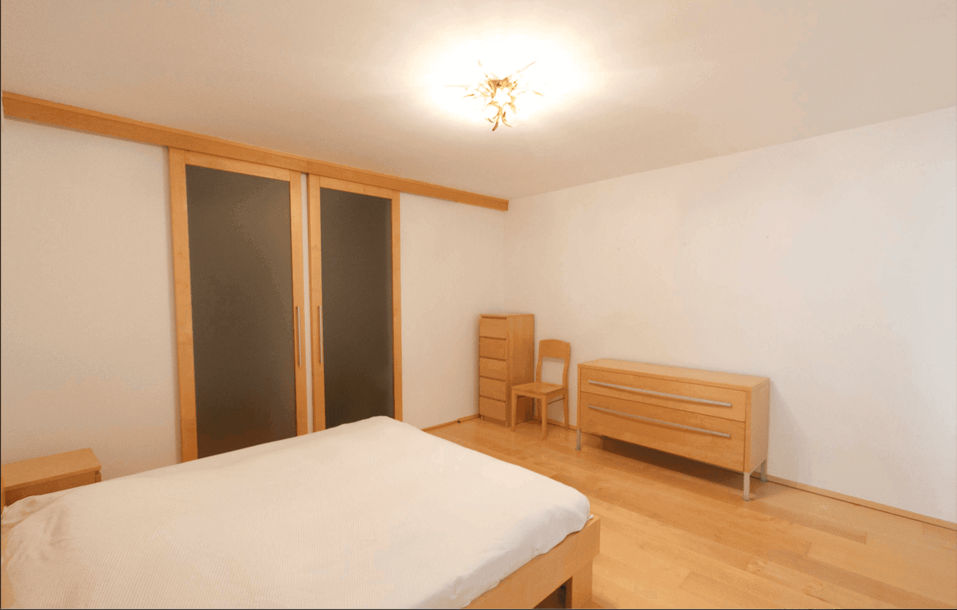 Schlafzimmer mit Holzbett, Kommoden und Schiebetüren, die zu einem begehbaren Kleiderschrank führen.