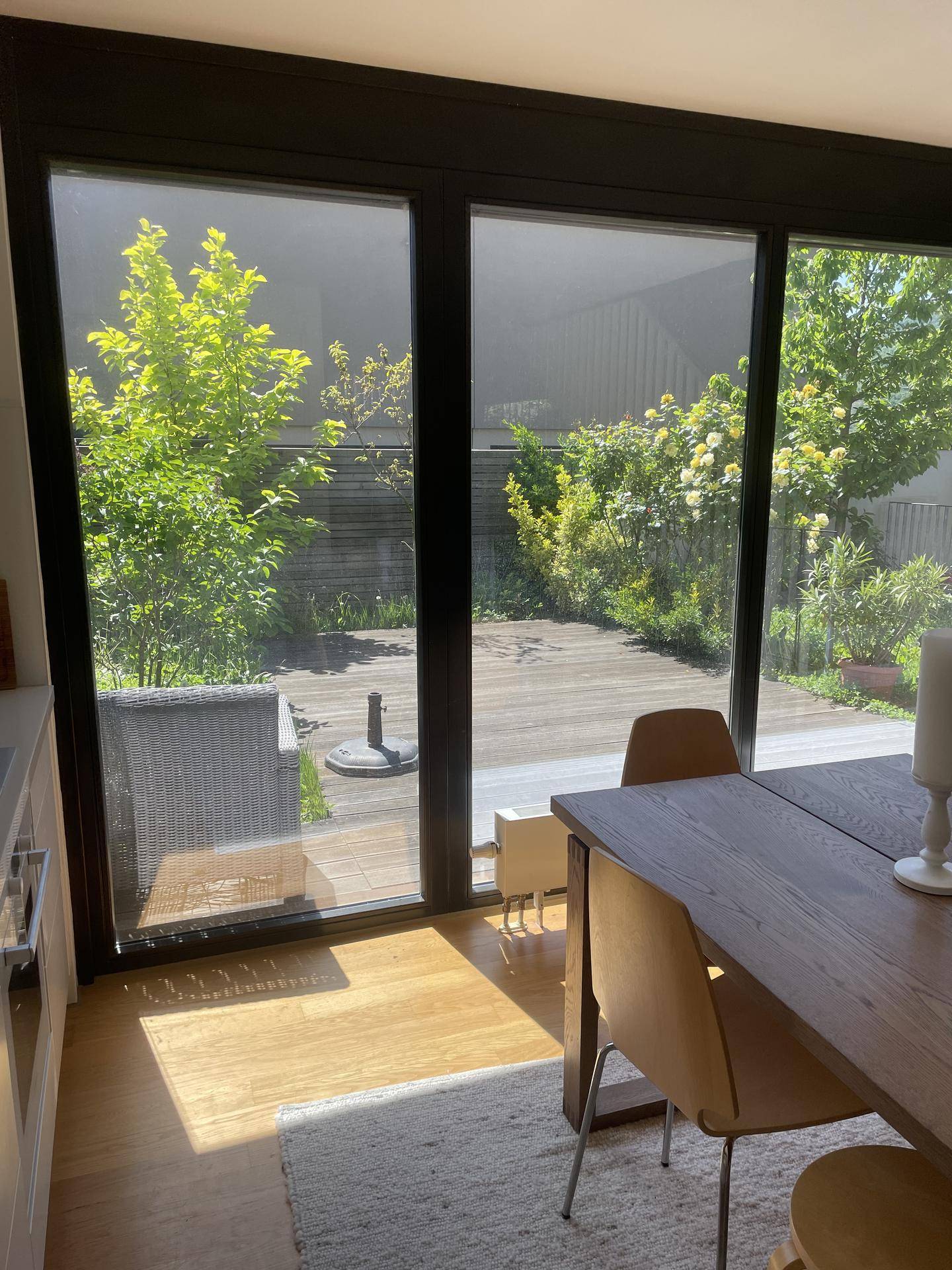 Heller Essbereich mit großen Glasfronten und direktem Zugang zu einer Holzterrasse und Garten.