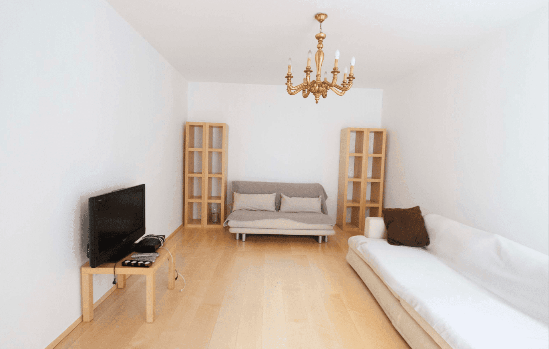Helles Wohnzimmer mit Parkettboden, zwei Sofas und einem goldenen Kronleuchter als Blickfang.