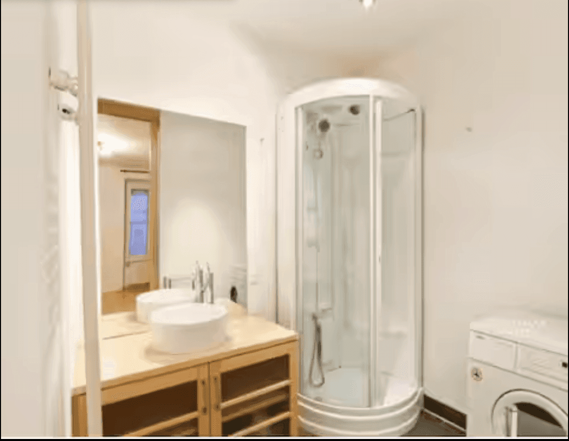 Funktionales Badezimmer mit Duschkabine, Waschbecken auf Holzunterschrank und integrierter Waschmaschine.