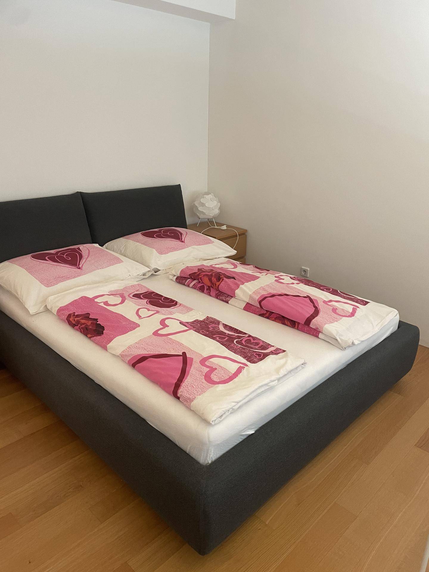 Schlafzimmer mit dunklem Polsterbett, farbenfroher Bettwäsche und einem kleinen Nachttisch.