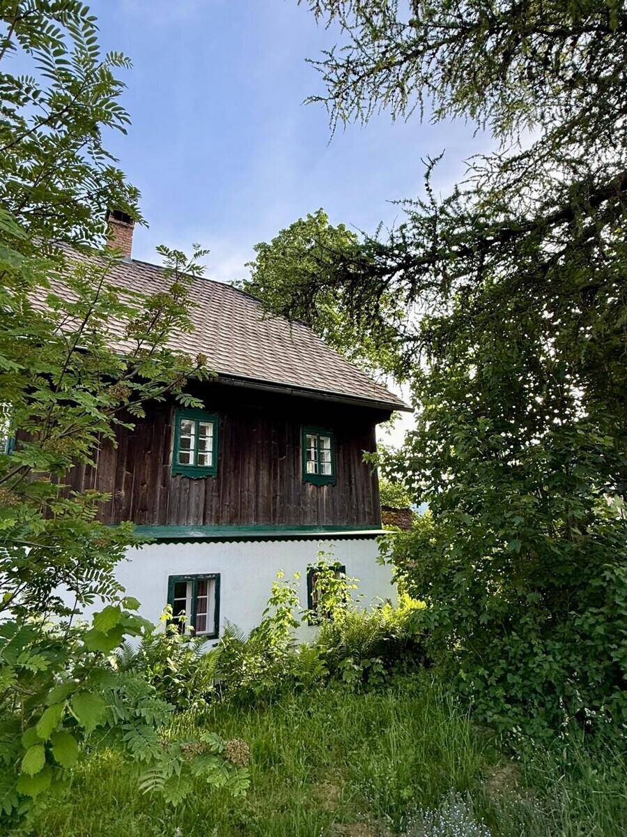 Detailansicht des Landhauses mit Holzelementen und grünen Fensterrahmen, umgeben von Bäumen.