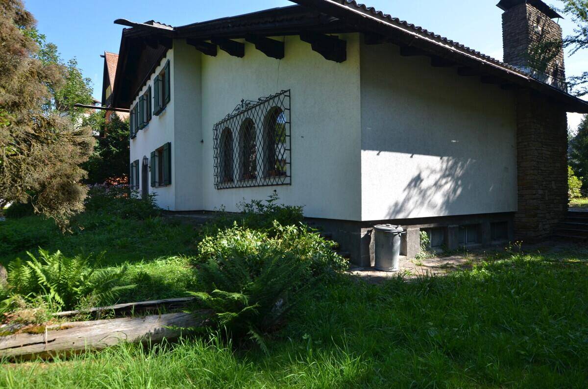 Seitenansicht des Hauses mit weißer Fassade, Steinmauer und üppigem Grün im Garten.
