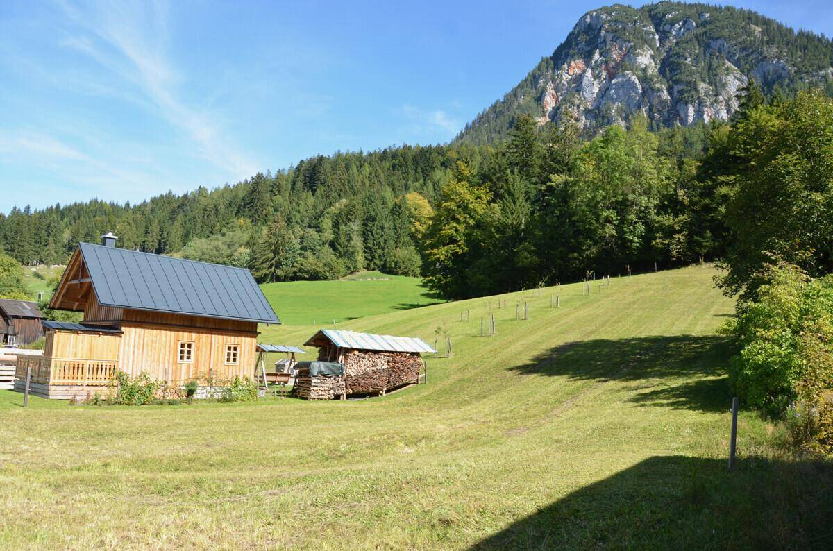 Traditionelles Holzhaus mit grauem Dach und einem Holzschuppen vor einer beeindruckenden Bergkulisse.