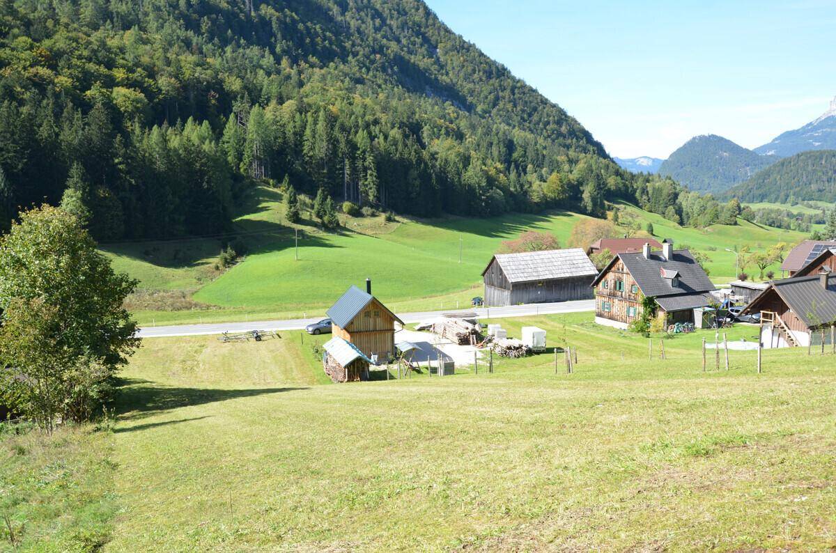 Malerische Berglandschaft mit traditionellen Holzhäusern, grünen Wiesen und einer Straße im Tal.