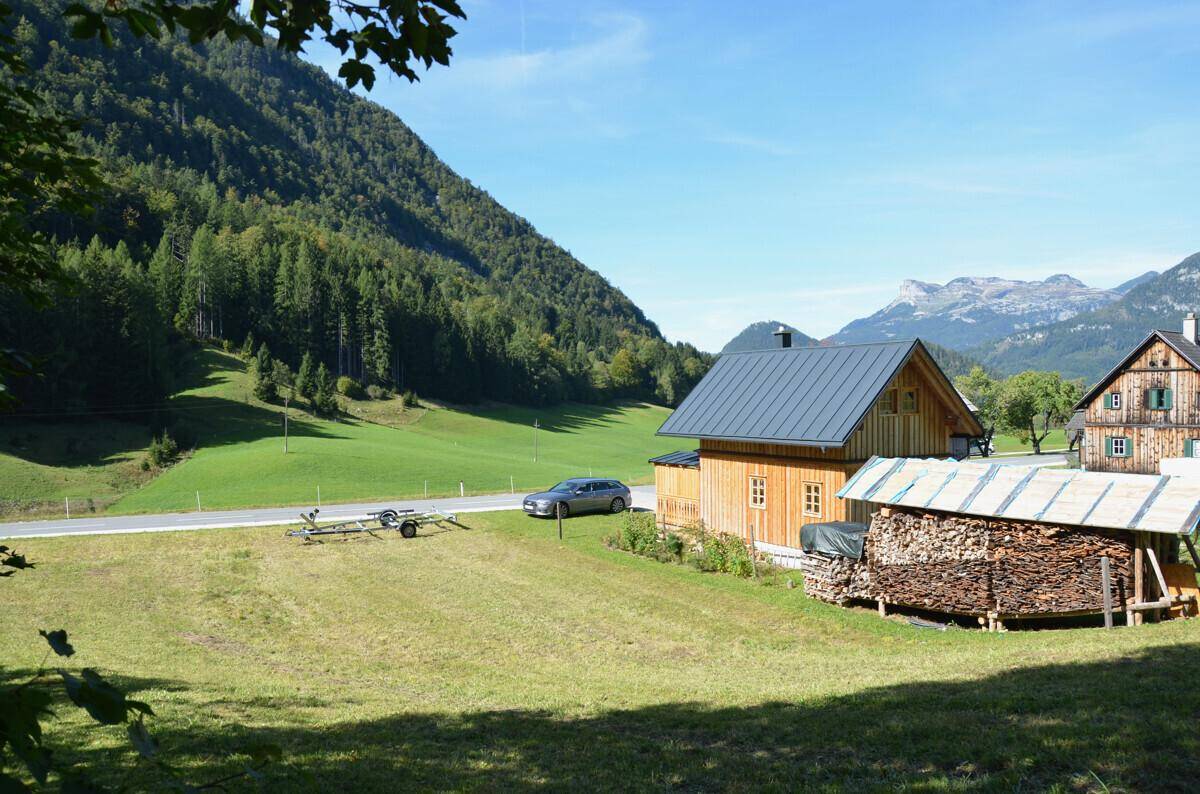 Idyllische ländliche Szene mit einem Holzhaus, einem Holzstapel und einer Bergstraße im Tal.