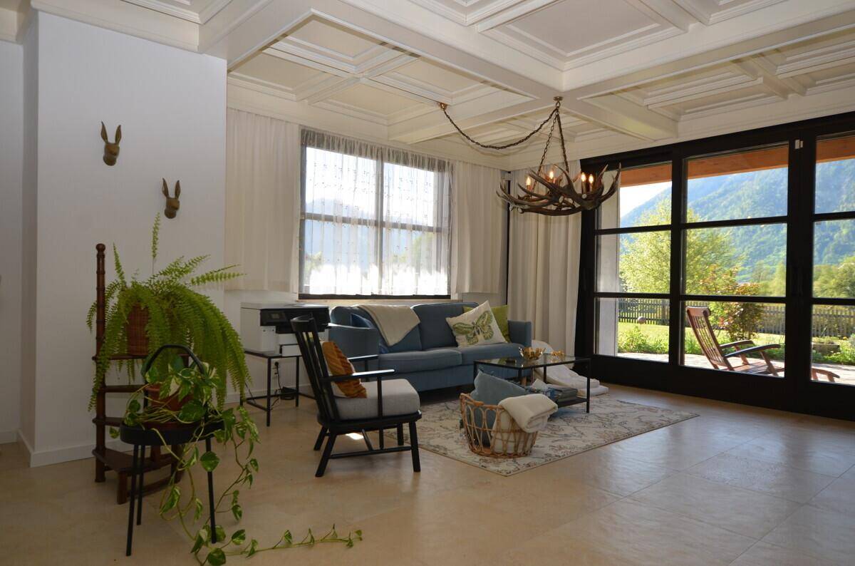 Geräumiges Wohnzimmer mit Kassettendecke, gemütlicher Sitzecke und direktem Zugang zur Terrasse mit Bergblick.
