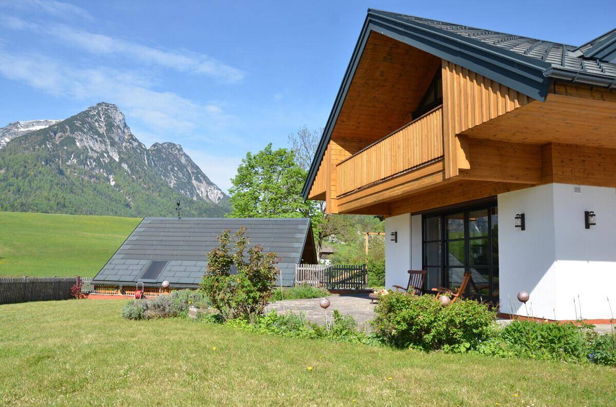 Ansprechendes Wohnhaus mit Nebengebäude und Garten vor einer malerischen Bergkulisse.