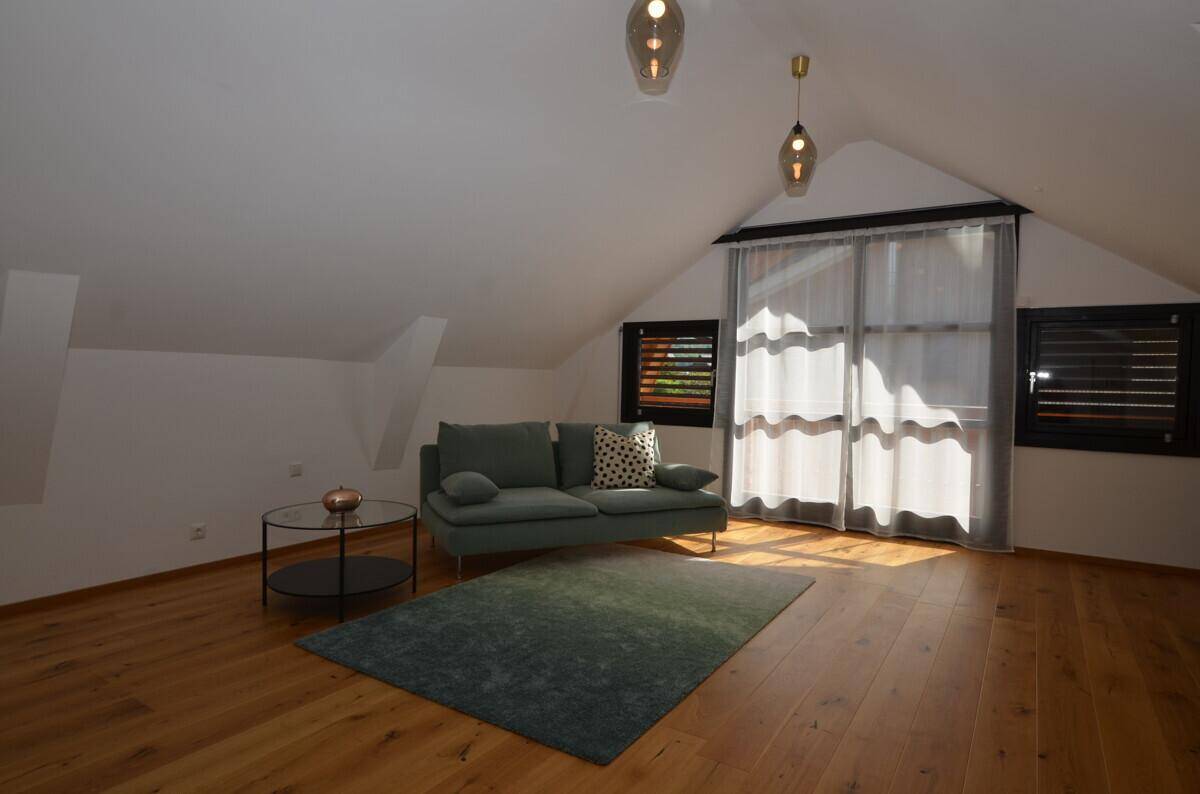 Heller Wohnbereich im Dachgeschoss mit grünem Sofa, Holzboden und Dachschrägen.