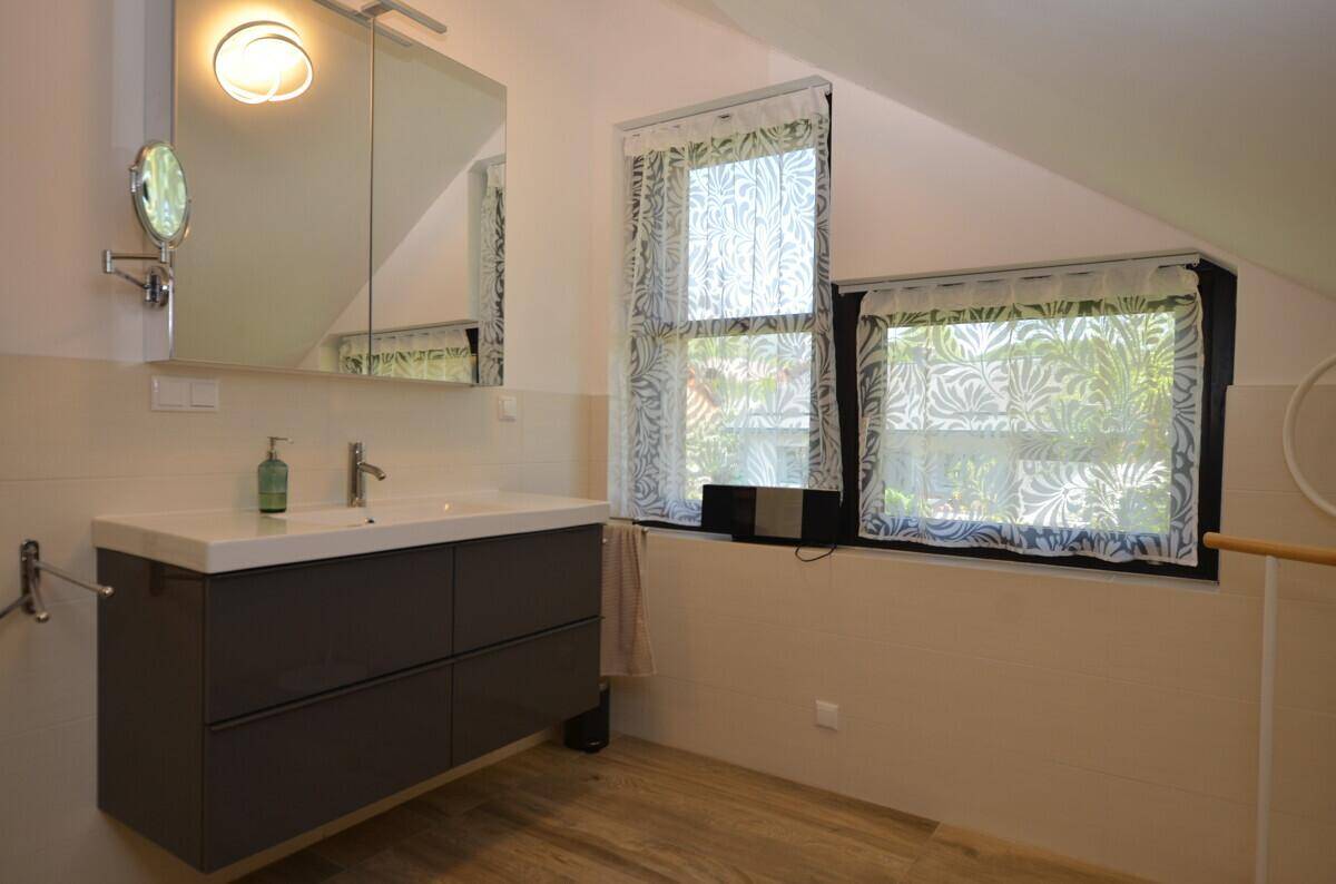 Helles Badezimmer mit modernem Waschtisch, Spiegelschrank und zwei Fenstern.