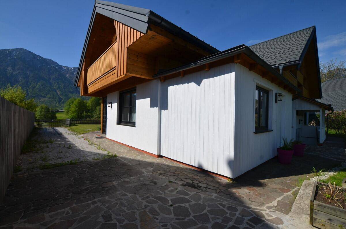 Modernes Haus mit Holzbalkon, weißer Fassade und Bergblick in sonniger, ländlicher Umgebung.