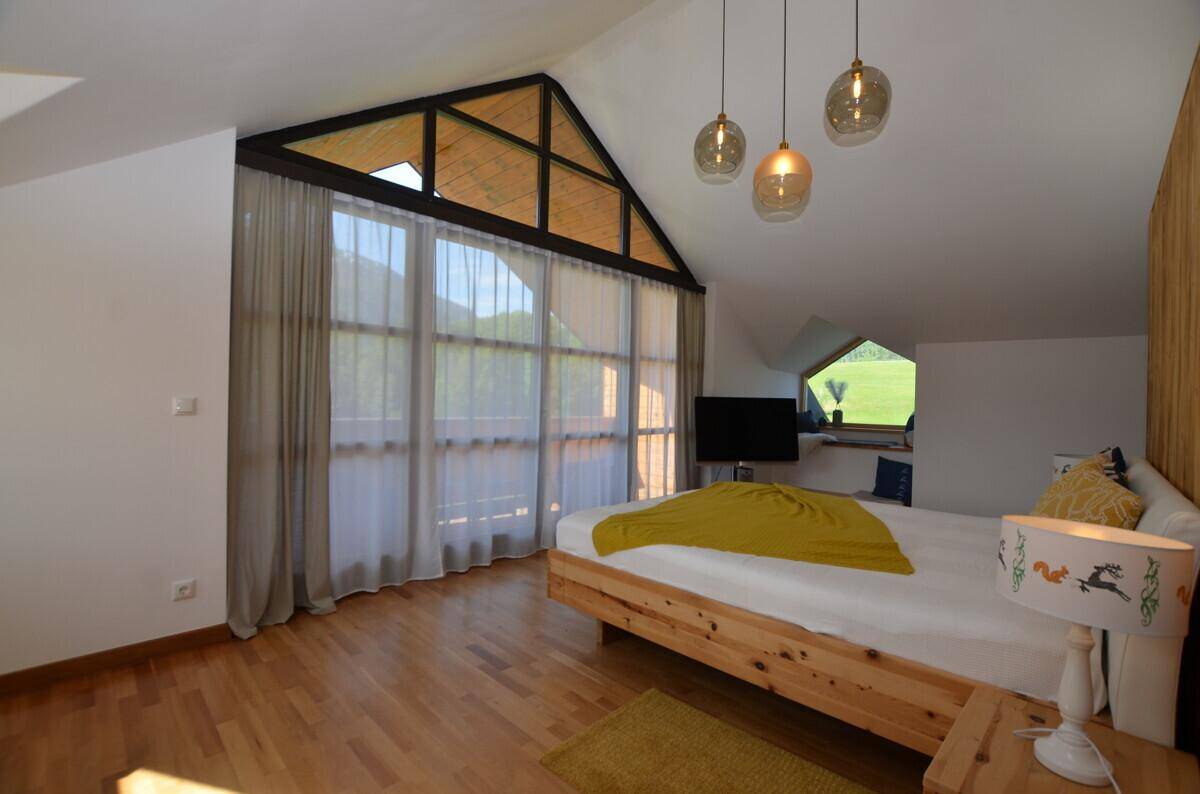 Helles Schlafzimmer mit Holzbett, Parkettboden und großen Fenstern mit Bergblick.