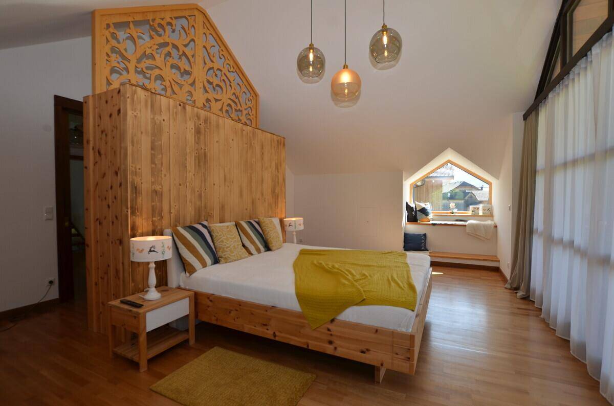 Geräumiges Schlafzimmer mit Holzbett, dekorativer Holzwand und gemütlicher Fensternische mit Bergblick.