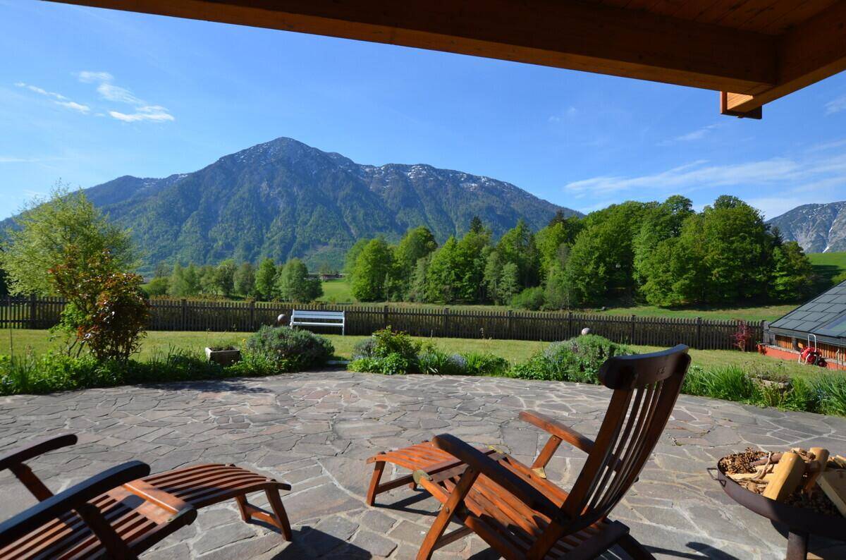 Sonnige Terrasse mit Steinplatten, Holzliegen und beeindruckendem Panoramablick auf die Berge.