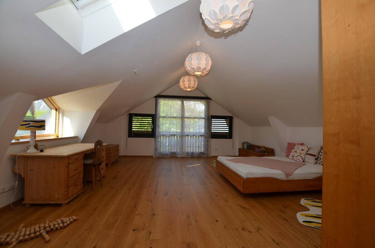 Gemütliches Schlafzimmer im Dachgeschoss mit Holzboden, Schreibtisch und Dachfenster.