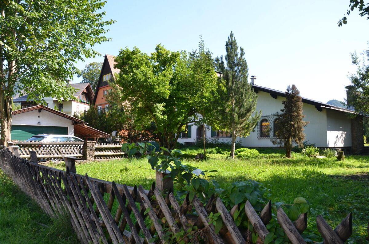 Ländliche Ansicht des Hauses mit Holzzaun, Bäumen und einem weiteren Gebäude im Hintergrund.