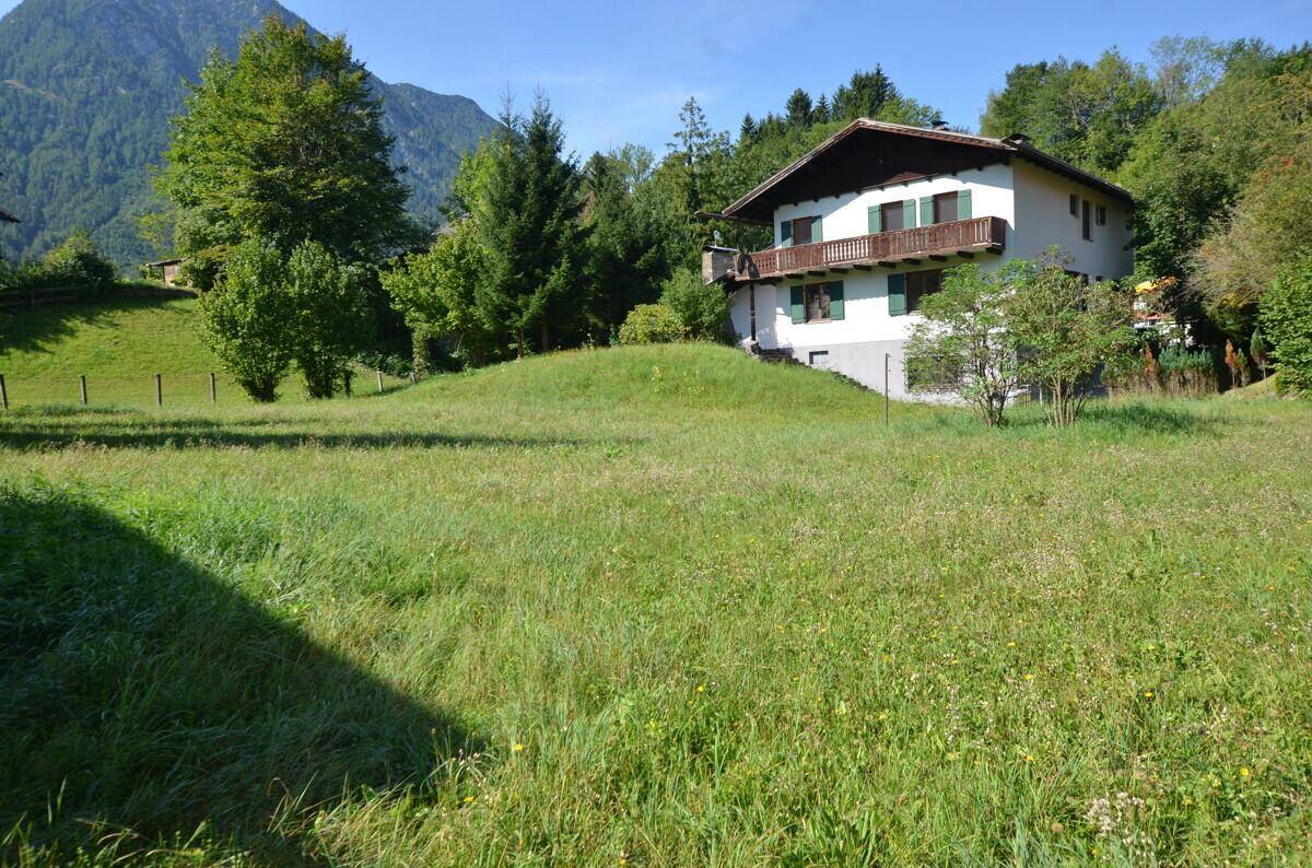 Großzügiger Gartenbereich mit weitläufiger Rasenfläche und Blick auf das Haus und die Berge.