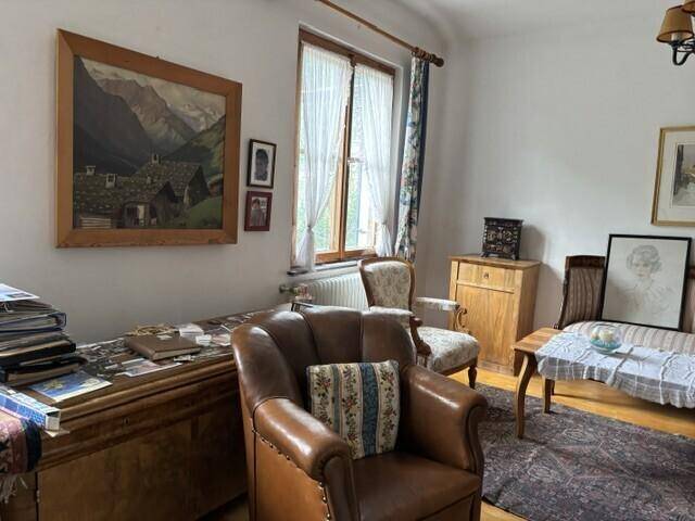 Traditionell eingerichtetes Wohnzimmer mit Ledersessel, Holztruhe und Kunstwerken an der Wand.