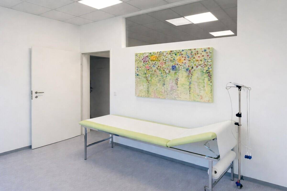 Heller Untersuchungsraum mit Liege, Kunstwerk an der Wand und funktionaler Ausstattung.