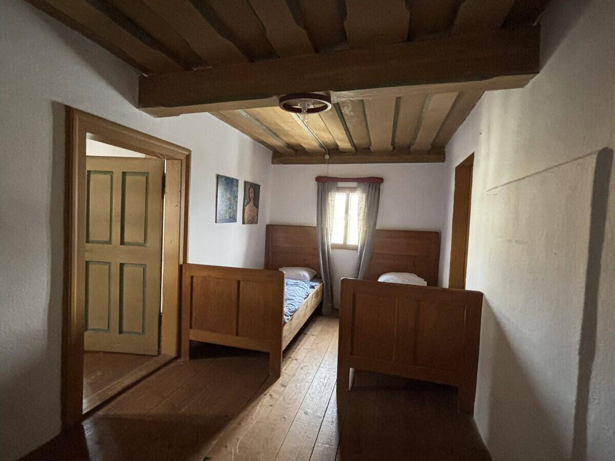 Schlafzimmer mit zwei Einzelbetten, Holzboden und sichtbaren Deckenbalken.