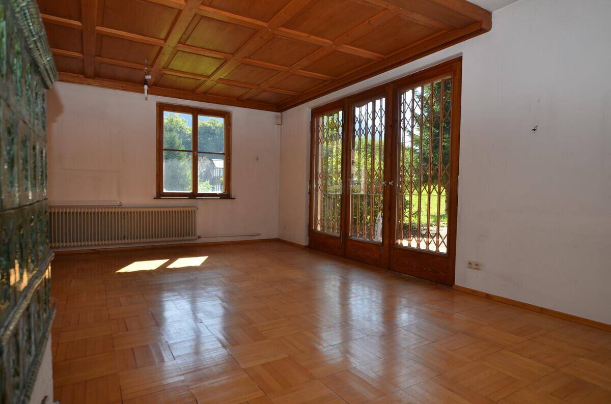 Geräumiges Wohnzimmer mit Parkettboden, Holzkassettendecke und Zugang zum Garten.