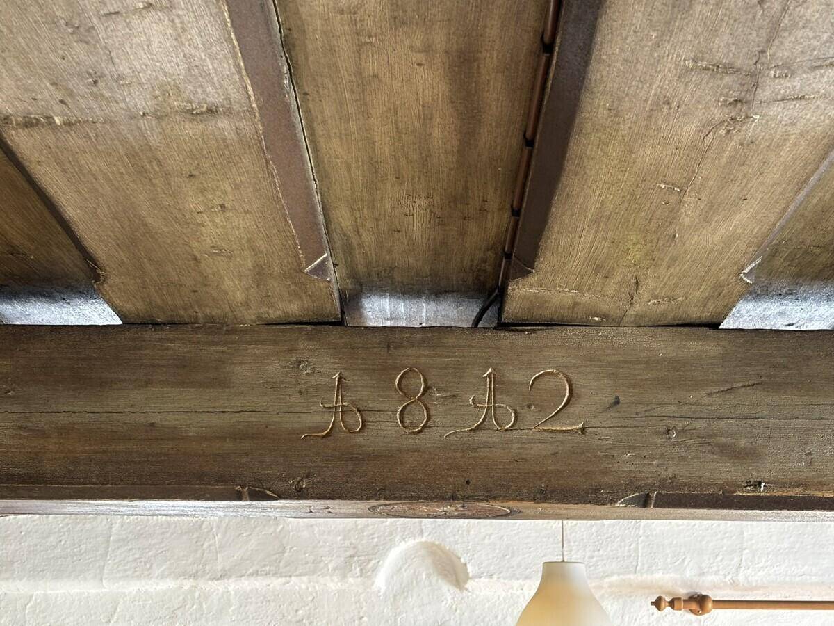 Nahaufnahme eines alten Holzbalkens mit eingravierter Jahreszahl 1812, Teil der Deckenkonstruktion.
