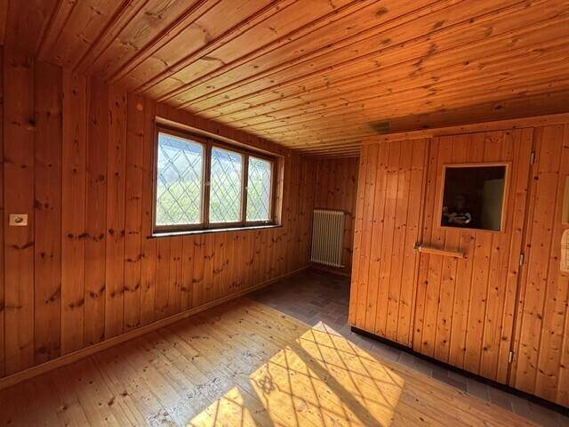 Raum mit Holzvertäfelung an Wänden und Decke, sowie einem Fenster mit Gittermuster.