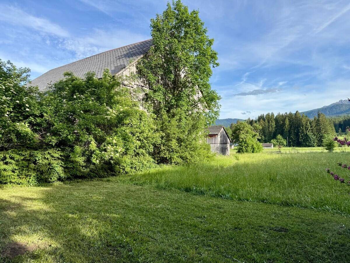 Weitläufige Grünfläche neben dem Landhaus mit Blick auf die umliegende Natur und Berge.