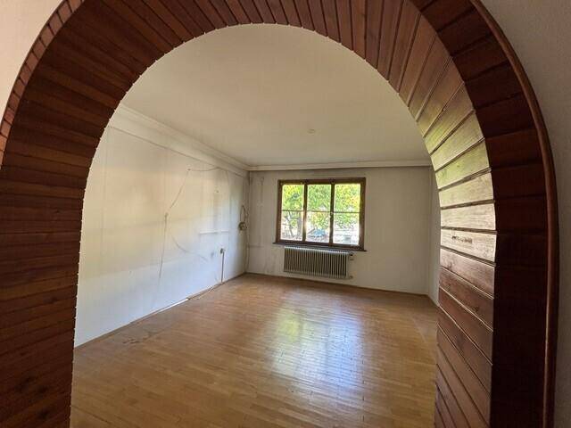 Leeres Zimmer mit Parkettboden und einem dekorativen Holzbogen als Durchgang.