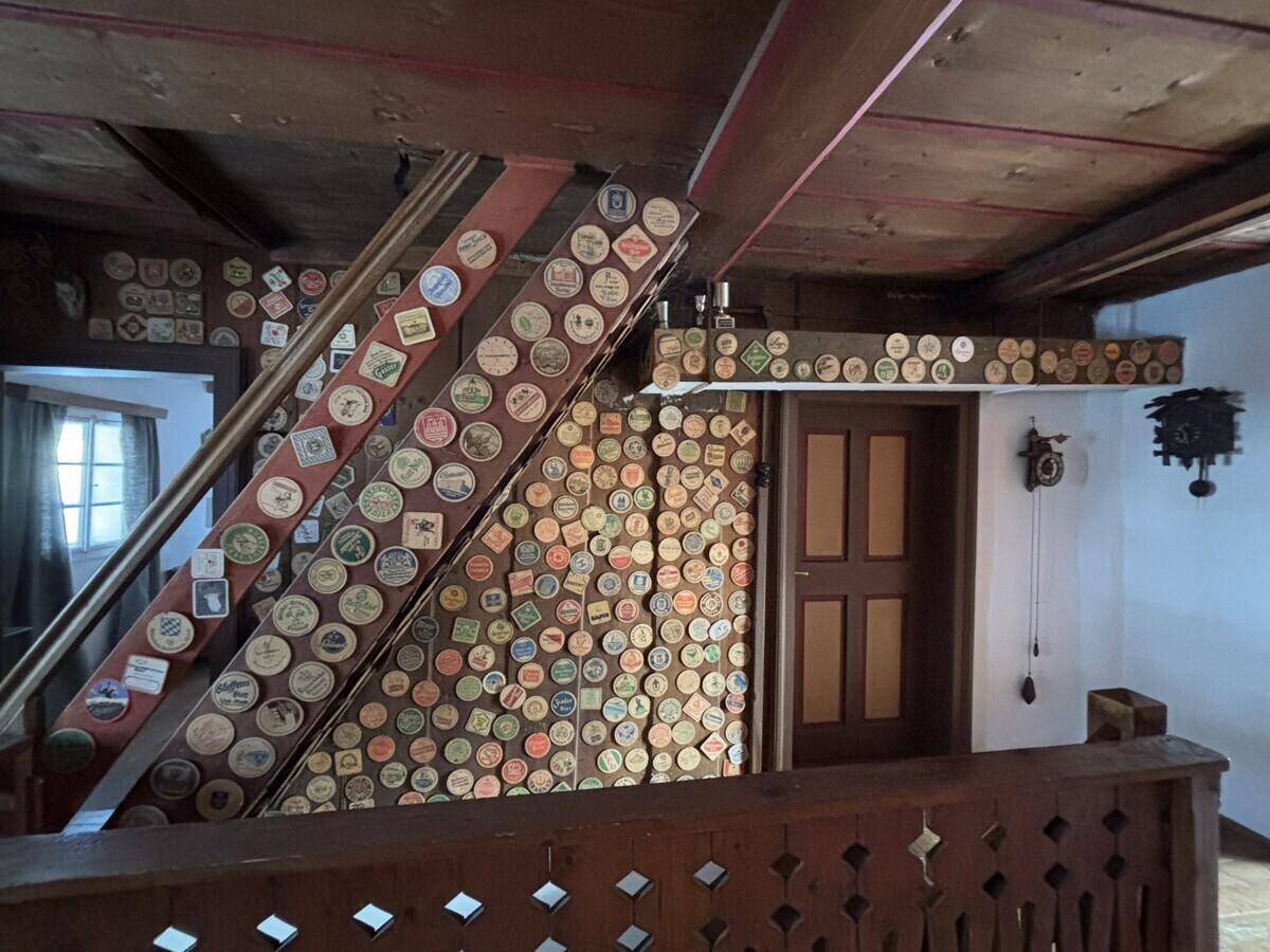 Treppenaufgang mit vielen Bierdeckeln an der Wand und rustikalem Holzgeländer.