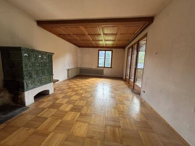 Helles Wohnzimmer mit Parkettboden, Holzkassettendecke und einem traditionellen Kachelofen.
