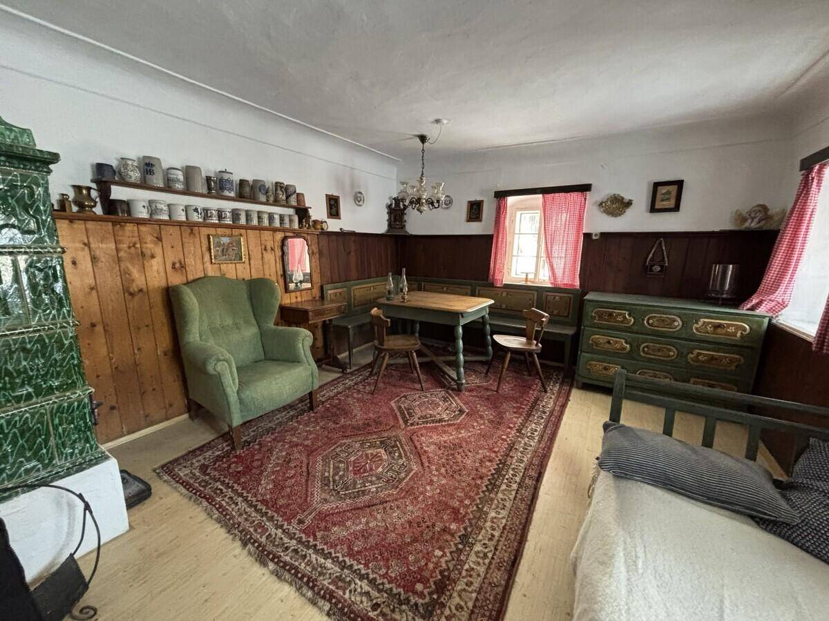 Geräumiger Wohnbereich mit Kachelofen, Holztäfelung, rustikalen Möbeln und einem Bett.