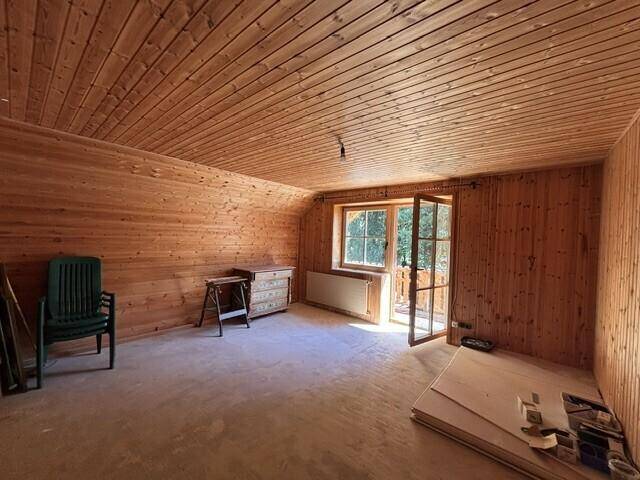 Helles Zimmer mit Holzvertäfelung an Wänden und Decke sowie Zugang zu einem Balkon.