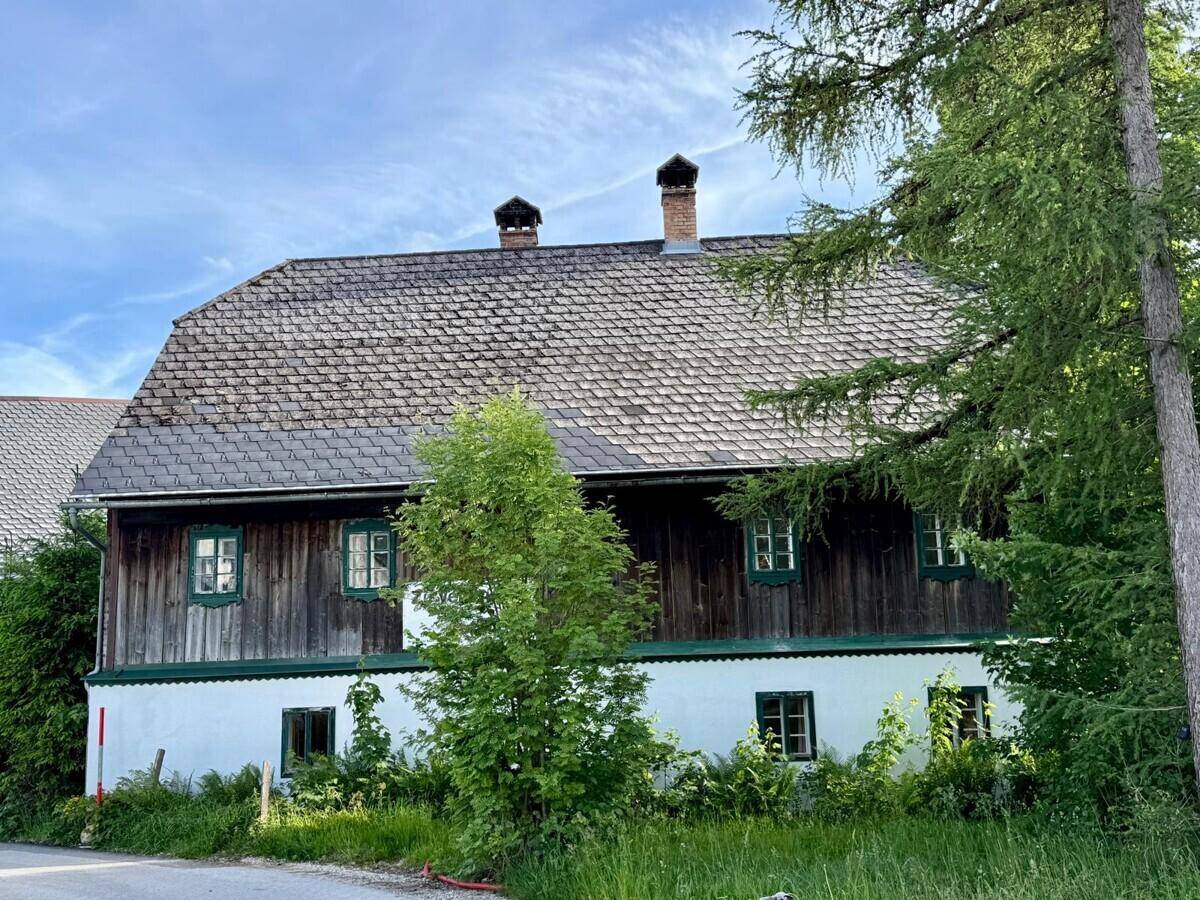 Rückansicht des traditionellen Landhauses mit Holzelementen, weißer Fassade und Satteldach.