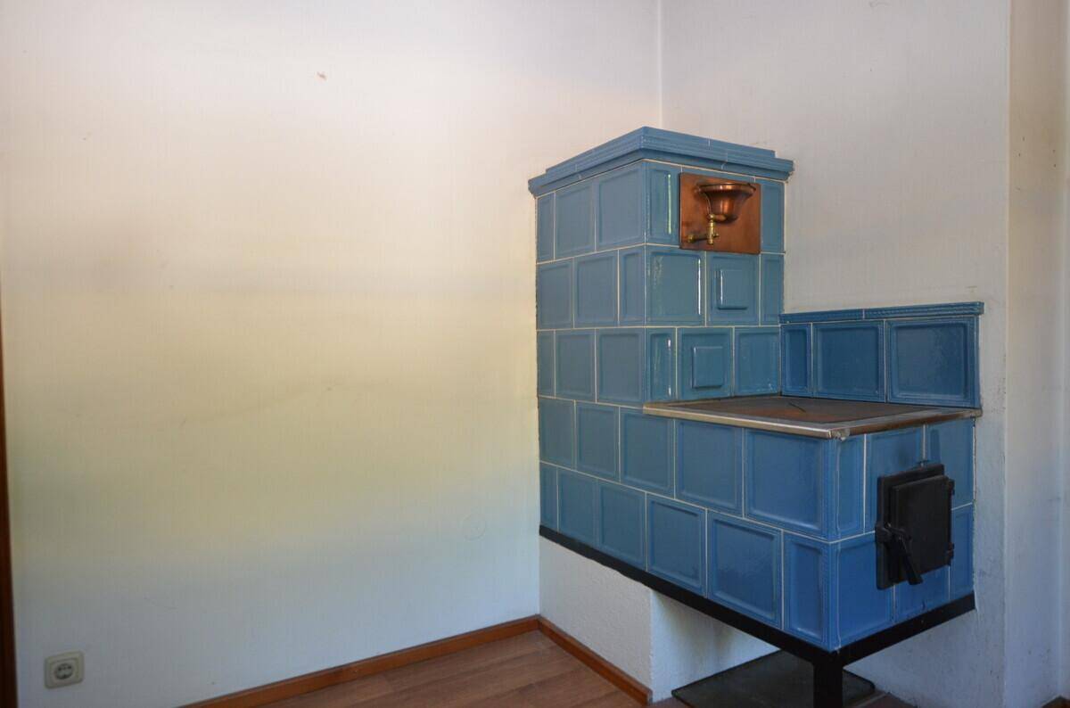 Blauer Kachelofen in einem hellen Raum mit Holzboden und weiß gestrichenen Wänden.