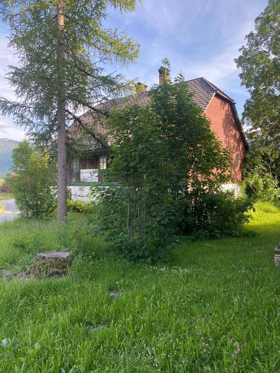 Seitenansicht des Landhauses mit roter Fassade und grüner Umgebung unter blauem Himmel.
