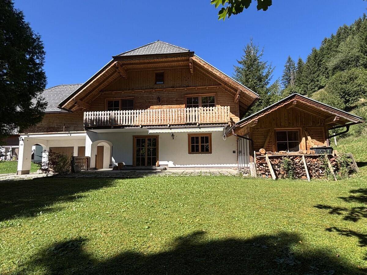 Großes Holzhaus mit angrenzendem Holzschuppen und weitläufigem Rasen in sonniger Lage.