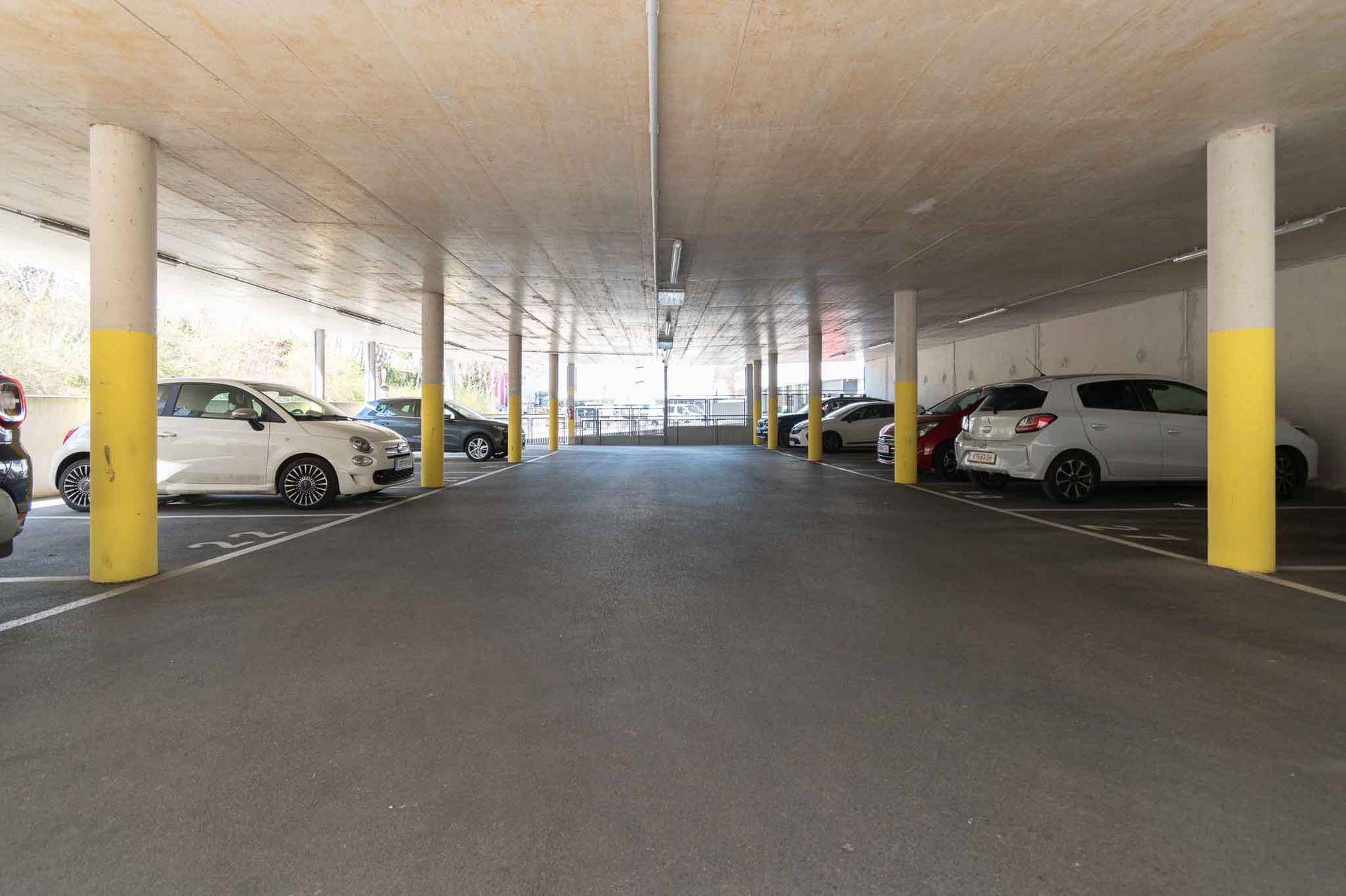 Weitläufige Tiefgarage mit markierten Parkplätzen und Autos unter einer Betondecke.